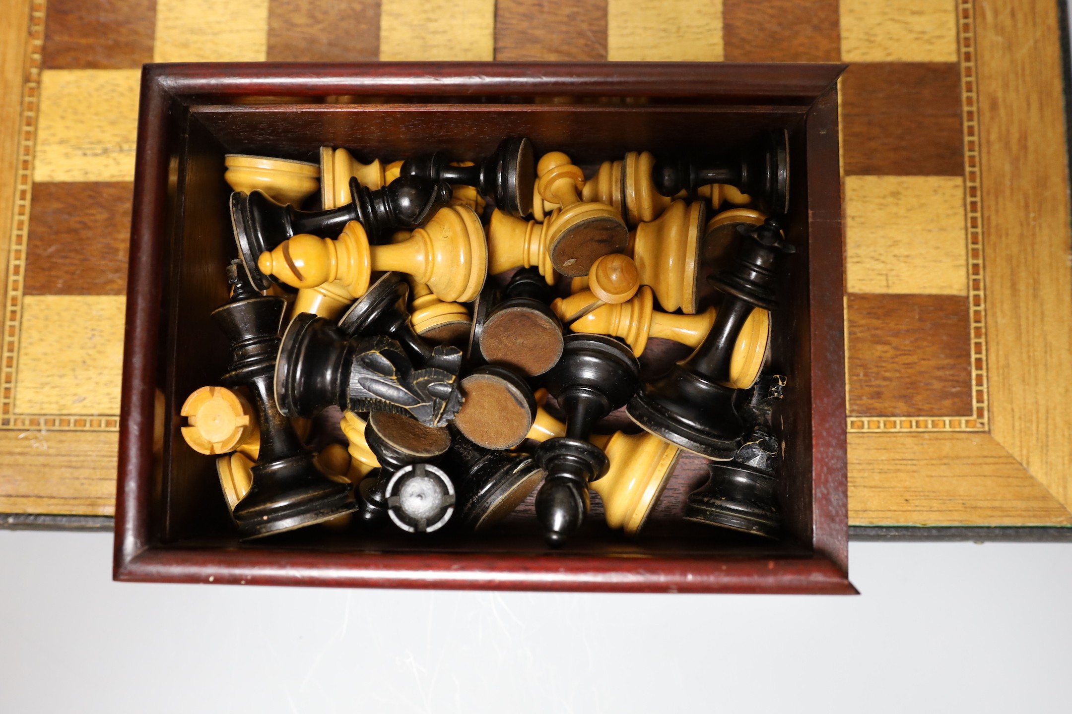 Two complete wood carved cased chess set pieces, king: 8cm and 7.5cm tall, together with a playing board